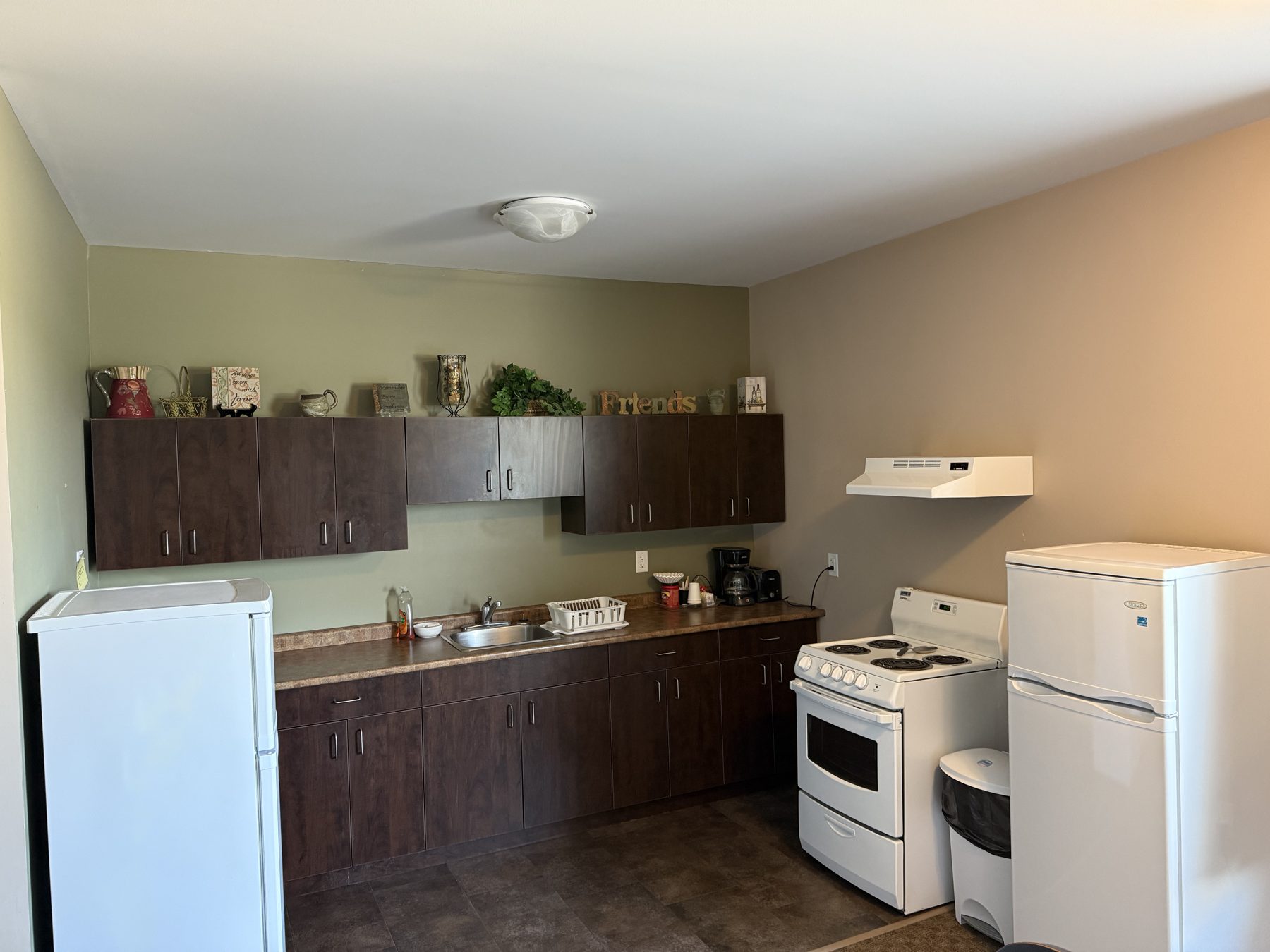 Kitchen area in the kitchenette room at Moosehorn Motor Hotel with stove, fridge, sink, coffee maker and cupboards
