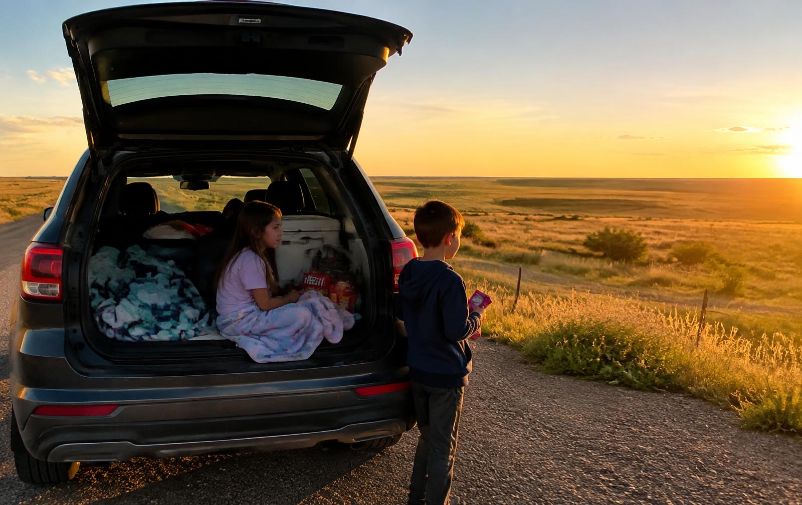 Children resting in the back of a packed car at a prairie roadside pull-off