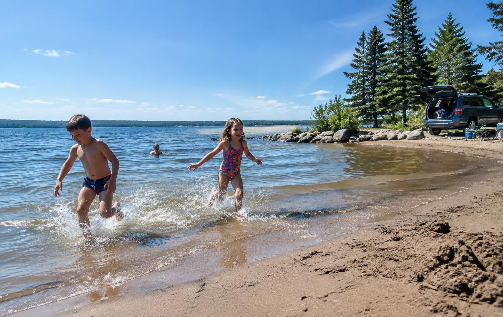 Children splashing at a lake beach on a summer family road trip