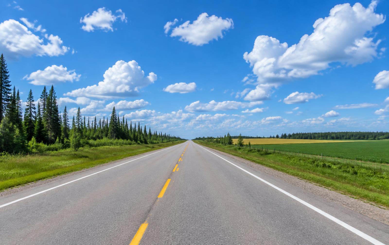 Straight summer highway through forest and farmland under a blue sky
